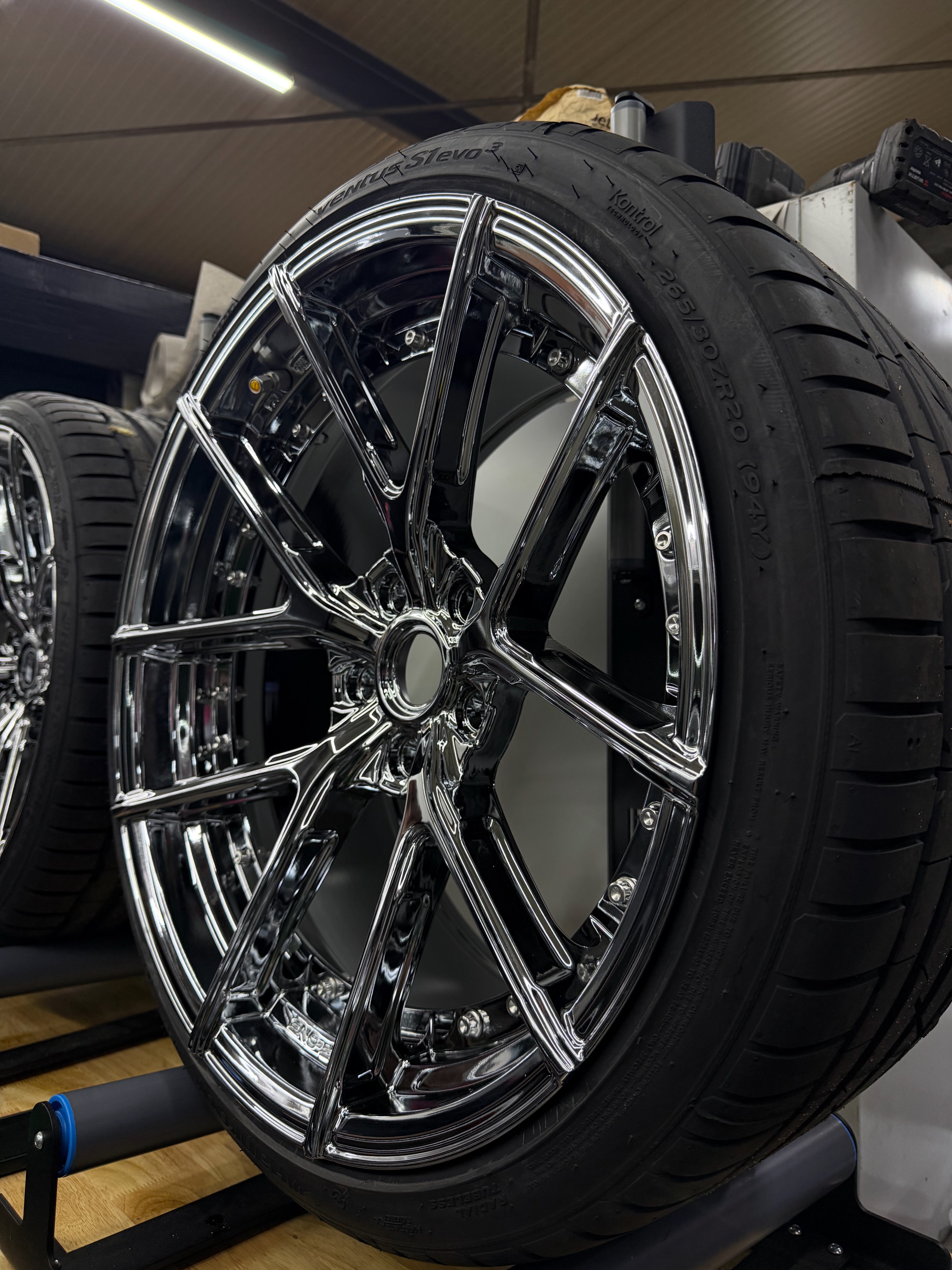 C² Wheel Ceramic Stage 2 — Chrome alloy wheel inspected on stand under high-intensity detailing lights showing mirror reflection